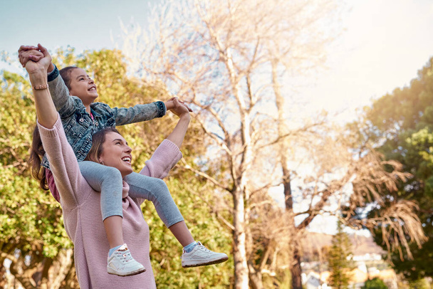 Family, woman and girl in park for piggyback, playing or bonding together with smile. Happy people, parent or mom with daughter outdoor in nature with energy, recreation or physical activity for fun. - Photo, Image
