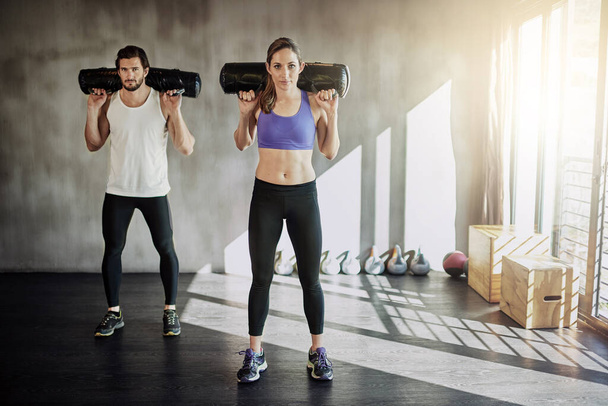 Man, woman and sandbag workout or gym exercise for healthy muscle fitness, weights or strength. Personal trainer, friends and athlete equipment or power teamwork with support, discipline or class. - Photo, Image