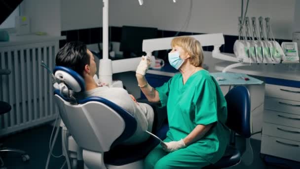 inyección general en una clínica dental un paciente con un dentista femenino que sostiene un espejo y consulta - Imágenes, Vídeo
