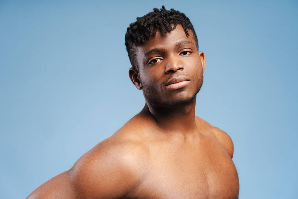Hezký, sexy, atraktivní Afroameričan bez trička muž dívající se na kameru pózující izolované na modrém pozadí. Pojetí sportu, reklama, nakupování - Fotografie, Obrázek