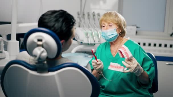 en una clínica dental un dentista le muestra al paciente cómo cepillarse los dientes correctamente - Imágenes, Vídeo