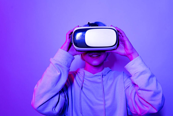 Kobieta z fioletowymi włosami nosi słuchawki VR i patrzy na ekran - Zdjęcie, obraz