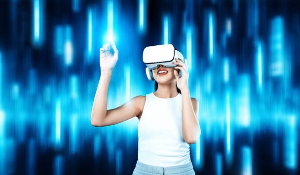 Vrouwelijke stand dragen witte VR-headset en mouwloze verbindende metaverse, toekomstige technologie, omgeven door abstract licht. Ze gebruikt index vinger aanraken hologram object van virtual reality. Hallucinatie. - Foto, afbeelding