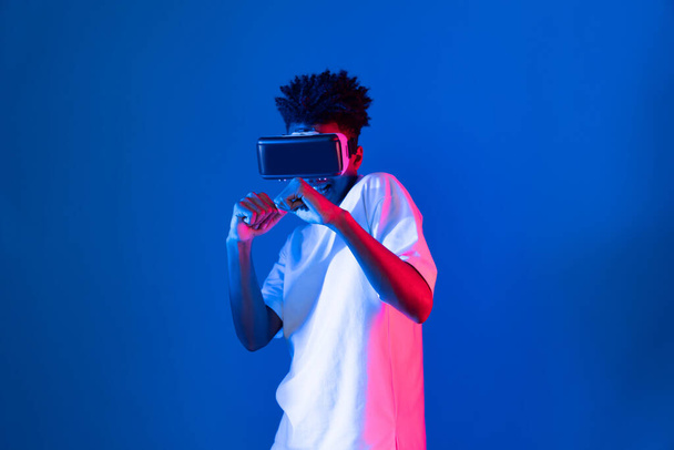 Afrikkalainen amerikkalainen nyrkkeily gamer yllään VR pelaa nyrkkeilijä peli booli kamera poseeraa eristetty sininen vaaleanpunainen neon valo seinä yhdistää futuristinen teknologia virtuaalitodellisuus metaverse taistelevat laatikko. Ennakko. - Valokuva, kuva