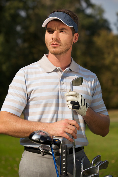 Young man standing by golf bag - Foto, imagen