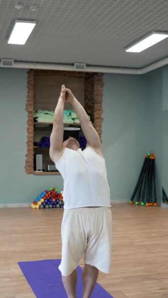 Giovane uomo pratica yoga in VR occhiali in piedi su stuoia blu messo sul pavimento in legno in studio. Persona di sesso maschile gode di realtà virtuale in formazione Colpo verticale. - Filmati, video