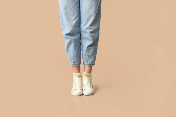 Piernas de mujer joven en zapatillas de deporte con estilo sobre fondo beige - Foto, Imagen