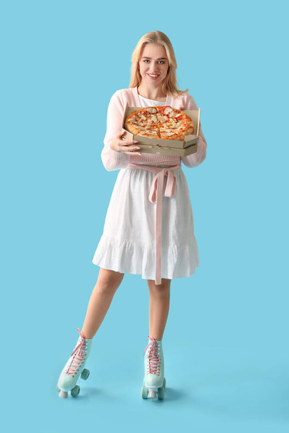 Young woman in roller skates holding tasty pizza on color background - 写真・画像