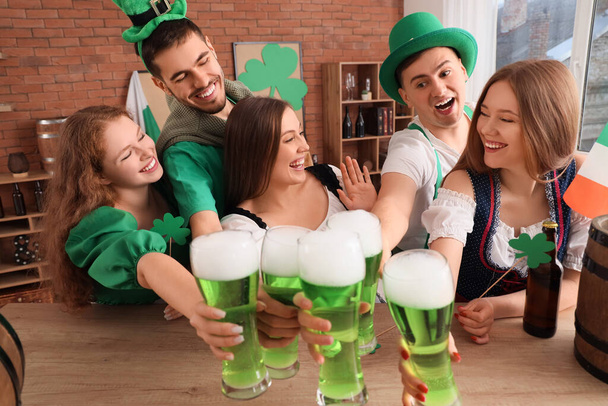 Group of young friends with beer celebrating St. Patrick's Day at table in pub - Foto, afbeelding