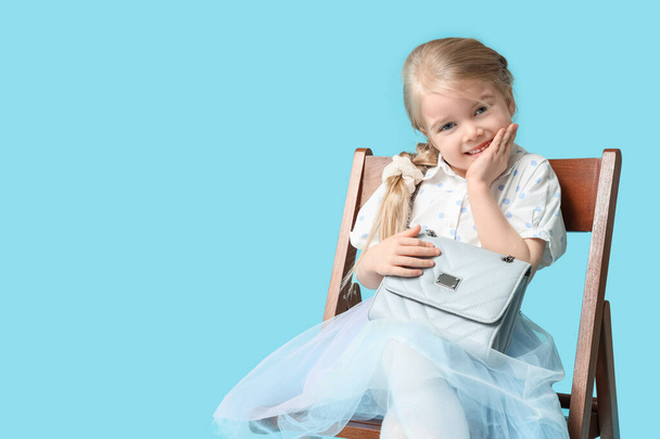 Cute little girl with stylish chain bag on chair against blue background - Foto, Imagem