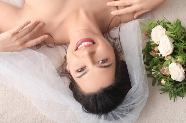 Beautiful young bride with wedding bouquet lying on bed, top view - Foto, imagen