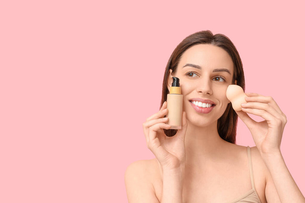 Beautiful young woman applying foundation by makeup sponge on pink background - Fotoğraf, Görsel
