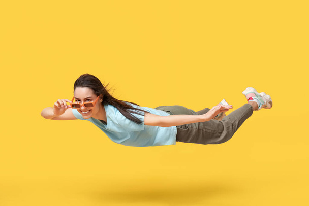 Gioiosa giovane donna in occhiali da sole che vola su sfondo giallo - Foto, immagini