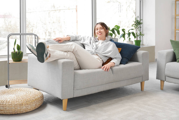 Щаслива молода жінка відпочиває на дивані вдома - Фото, зображення