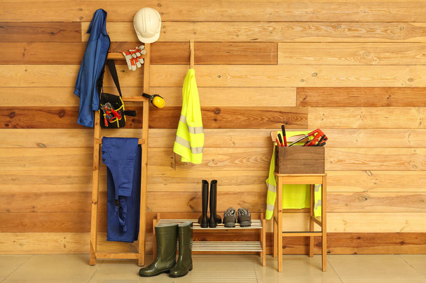 Chalecos de seguridad, uniformes, herramientas y calzado cerca de la pared de madera - Foto, imagen