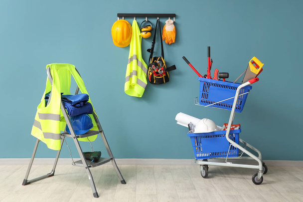 Stepladder, safety vests and pushcart with tools near blue wall - Photo, Image