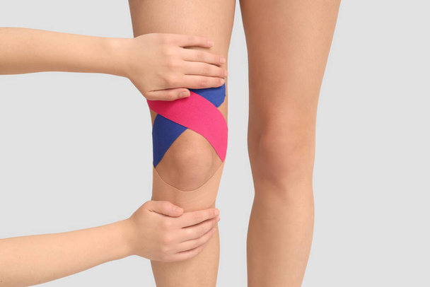 Physiotherapist applying tape onto woman's knee on white background, closeup - 写真・画像