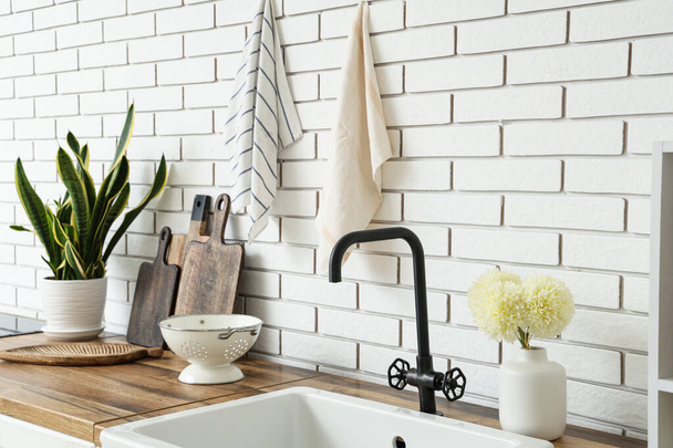 Ξύλινοι πάγκοι κουζίνας με νεροχύτη, σκεύη και houseplant κοντά σε λευκό τοίχο - Φωτογραφία, εικόνα