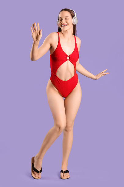 Femme heureuse en bikini avec écouteurs sur fond violet - Photo, image