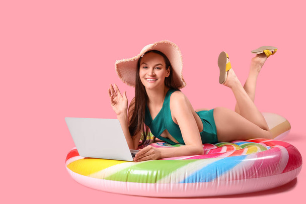 Smiling woman with laptop lying on inflatable mattress against pink background - Фото, зображення