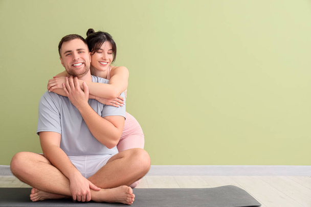 Sporty young couple sitting on yoga mat near green wall at home - Foto, imagen