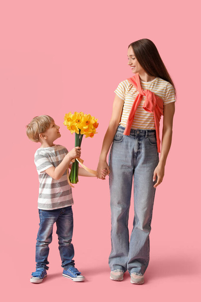 Happy woman and her little son with bouquet of beautiful narcissus on pink background - Fotografie, Obrázek