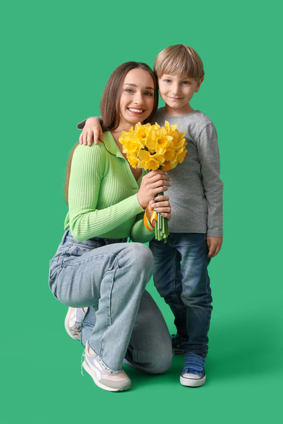 Happy woman and her little son with bouquet of beautiful narcissus on green background - Φωτογραφία, εικόνα