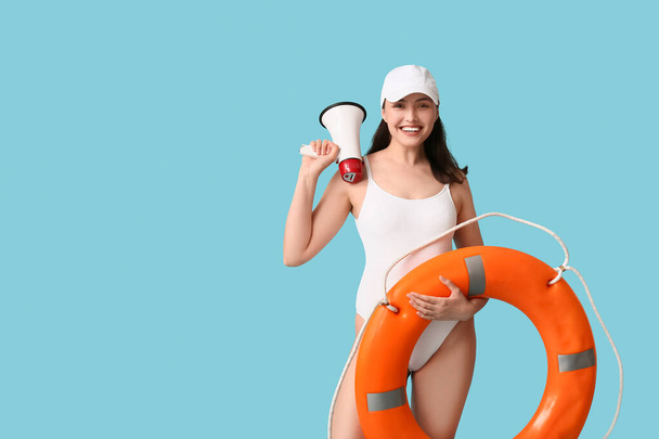 Young female lifeguard with ring buoy and megaphone on blue background - Foto, Bild