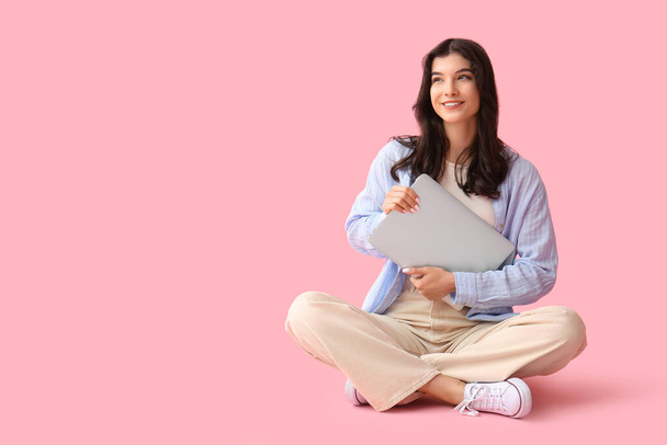 Beautiful young happy woman with laptop sitting on pink background - Fotó, kép
