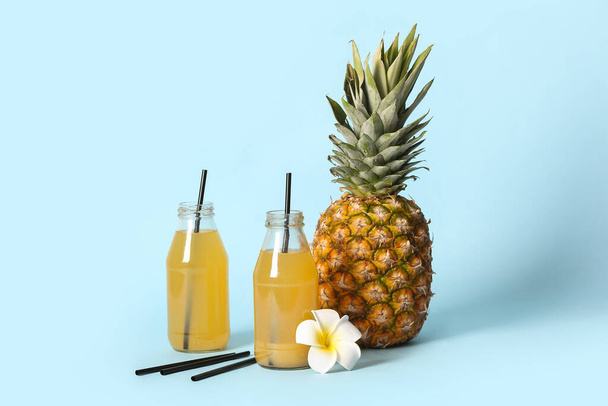 Свіжий стиглий ананас і пляшки смачного соку на синьому фоні - Фото, зображення