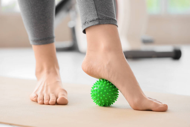 Sporty young woman massaging her foot with ball at gym, closeup - Photo, image