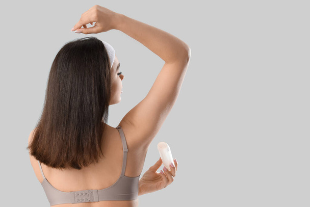 Young woman applying deodorant on light background, back view - Fotografie, Obrázek