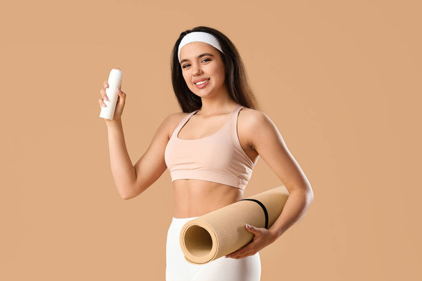 Young woman with deodorant and fitness mat on brown background - Fotoğraf, Görsel