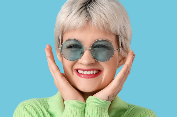 Portrait of beautiful young woman with sunglasses on blue background, closeup - Foto, Imagem