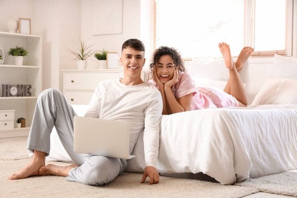 Happy young beautiful couple with laptop in bedroom - Φωτογραφία, εικόνα