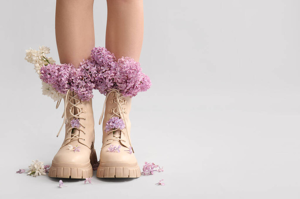 Legs of beautiful young woman in boots with lilac flowers on grey background - 写真・画像