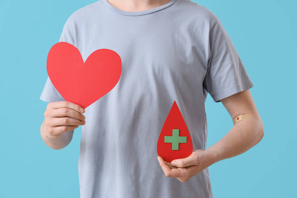 Male blood donor with paper heart and drop on blue background, closeup - Foto, Bild