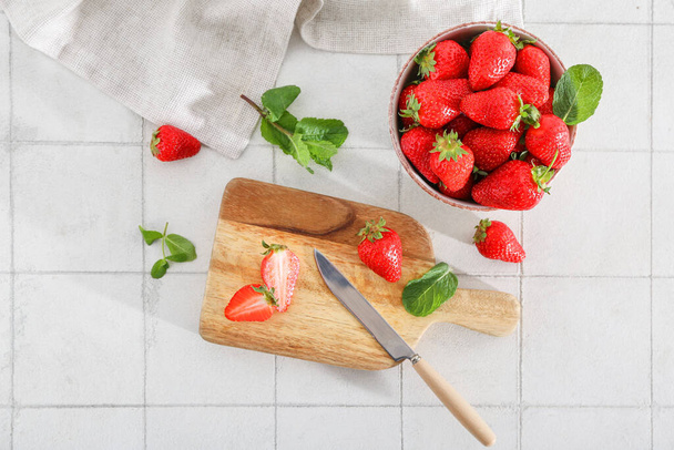 Tablero de madera y tazón con fresas frescas dulces sobre fondo de baldosas blancas - Foto, imagen