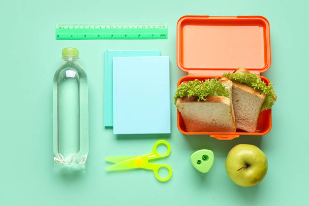 Lunchbox with sandwiches, bottle of water and stationery on color background - Photo, Image