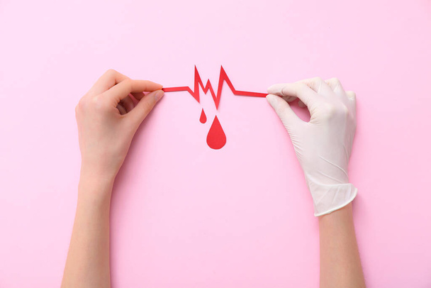 Female hands with cardiogram and paper blood drops on pink background. World Blood Donor Day - Fotó, kép
