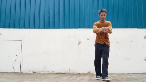 Hispanic man stretch arms and dance street dancing in front of wall. Motion shot of dancer or choreographer in casual outfit practicing b-boy dancing in hip hop style. Outdoor sport 2024. hiphop. - Footage, Video