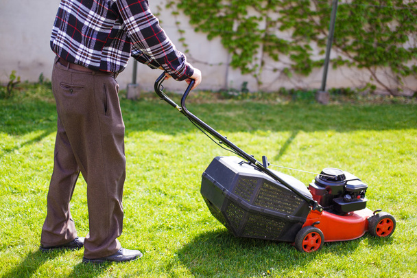 Eläkeläinen leikkaa nurmikkoa takapihalla
 - Valokuva, kuva