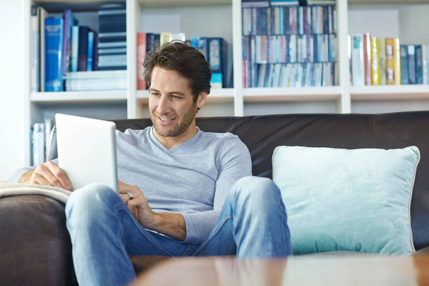 Mann, entspannen Sie sich und lächeln Sie auf dem Sofa mit Tablet für Internet-Streaming, Online-Spiele und soziale Medien im heimischen Wohnzimmer. Person, glückliche und digitale Technologie zum Lesen von E-Books, zur Websuche oder zum Stöbern auf der Couch. - Foto, Bild