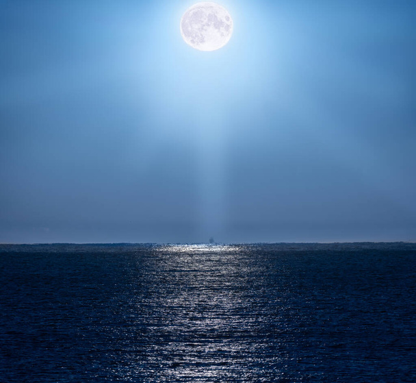 明るく青い夜空を照らす満月と,地中海海の水に美しく映し出され,地平線にバックライトの釣りボートを照らす光の光で. - 写真・画像