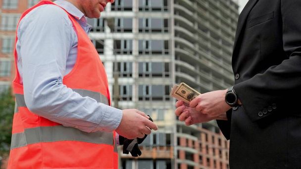 Управляющий строительством дает деньги строителю, пожимая руки возле незавершенного многоэтажного здания. Медленное движение - Фото, изображение