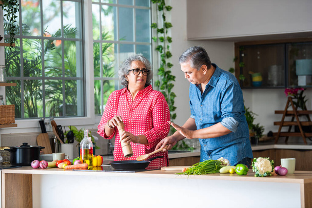 Senior Indian asian couple, cooking and having fun while preparing a healthy food in the kitchen at home - Photo, Image