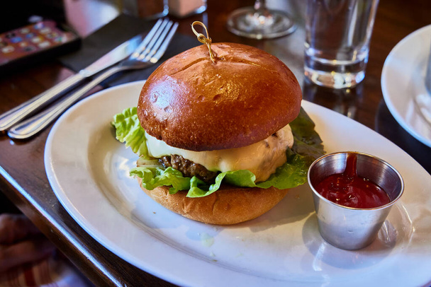 Een cheeseburger. Bord met een rundvlees hamburger, met kaas, sla en ketchup saus - Foto, afbeelding