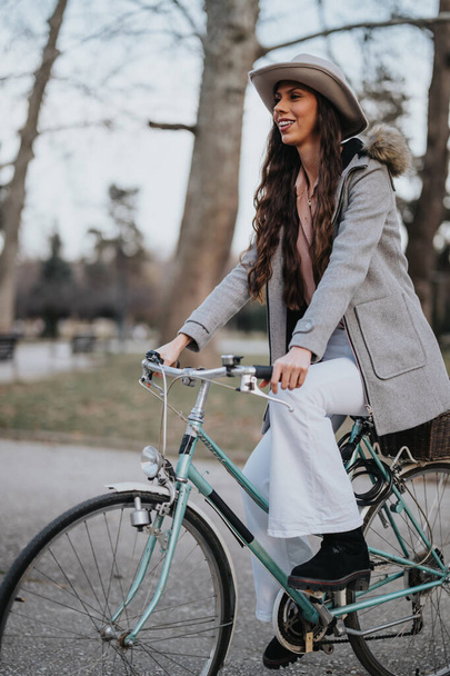 Een evenwichtige zakenvrouw geniet van een rustig moment met haar klassieke fiets in de sereniteit van een stadspark. - Foto, afbeelding