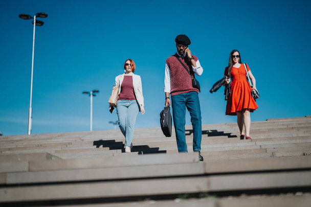 Три бизнес-работника поднимаются по ступенькам на улицу, демонстрируя сочетание профессионализма и случайного стиля - Фото, изображение