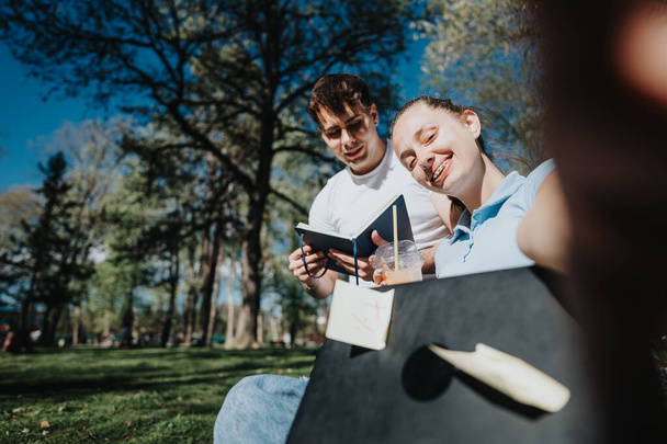 Dois alunos do ensino médio estudam juntos ao ar livre em um dia ensolarado, colaborando em um projeto com notas e tablet digital. - Foto, Imagem